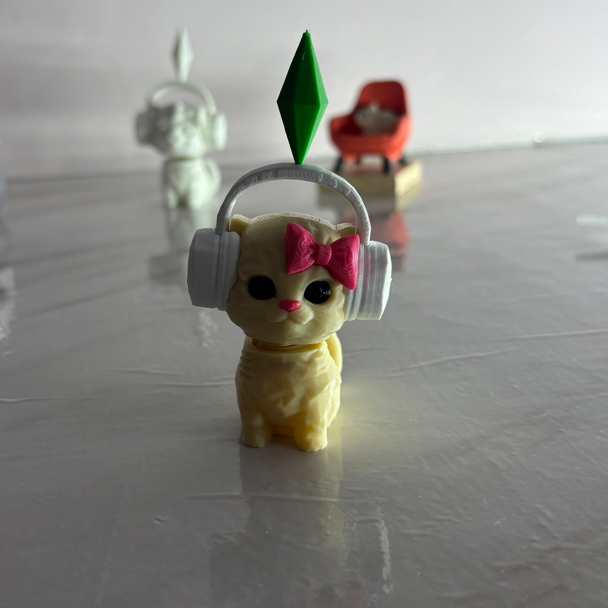Small yellow figurine with headphones and a pink bow on a reflective surface.