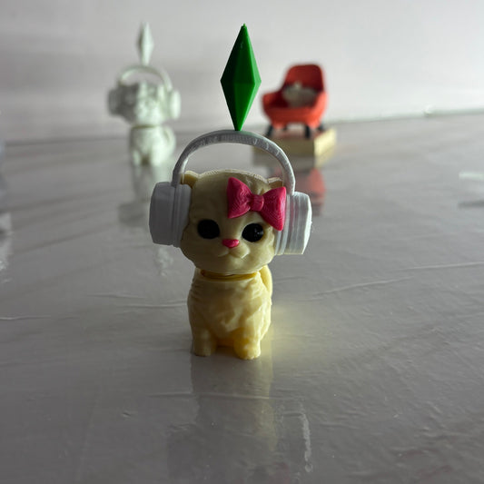 Small yellow figurine with headphones and a pink bow on a reflective surface.