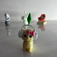 Small figurine of a cat wearing headphones with a pink bow on a reflective surface.