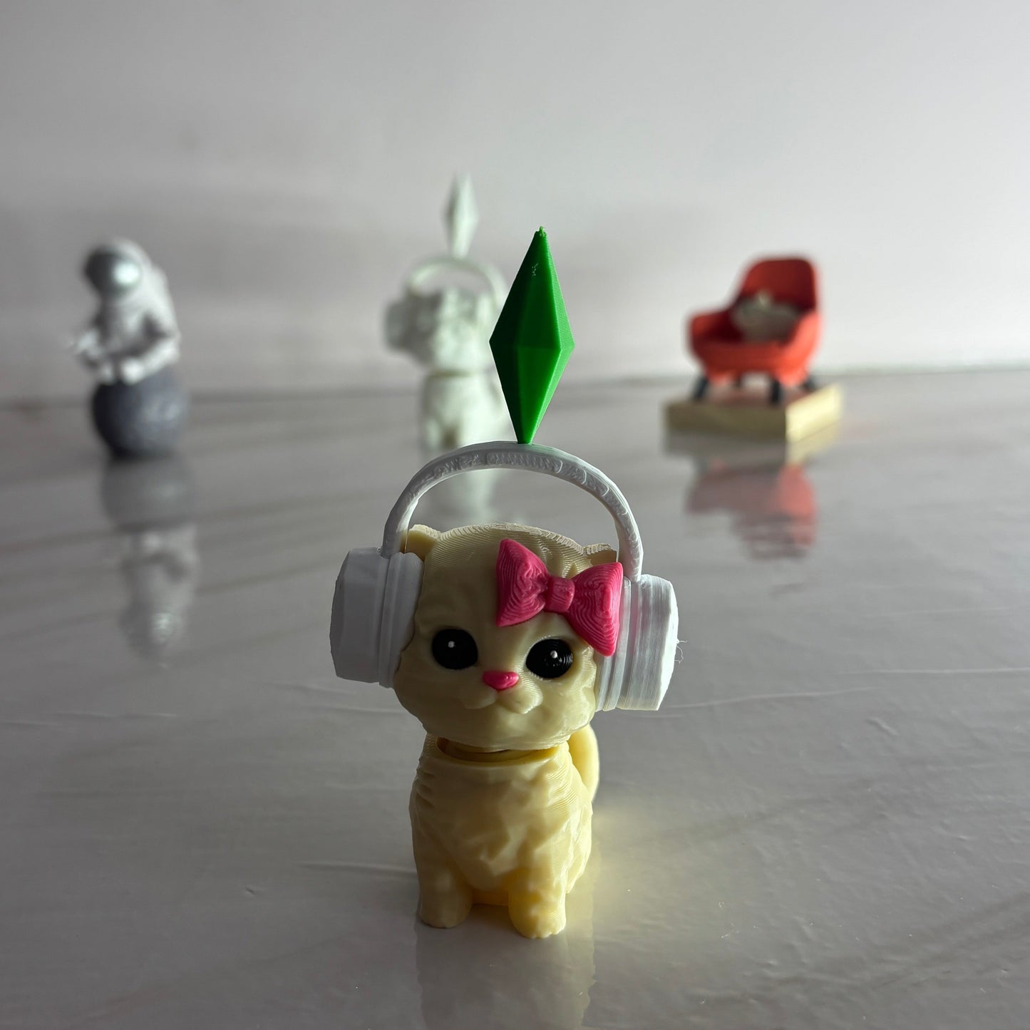 Small figurine of a cat wearing headphones with a pink bow on a reflective surface.