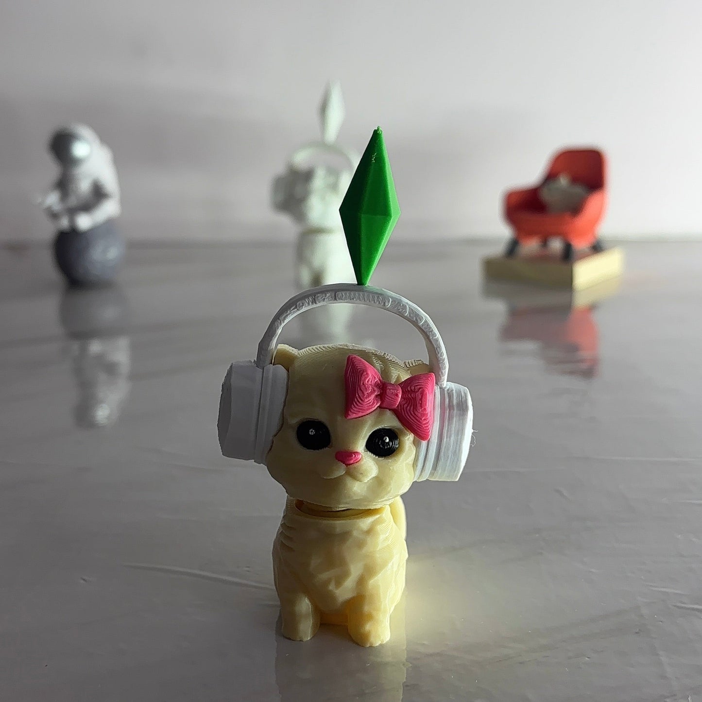 Small figurine of a cat wearing headphones with a pink bow on a reflective surface.