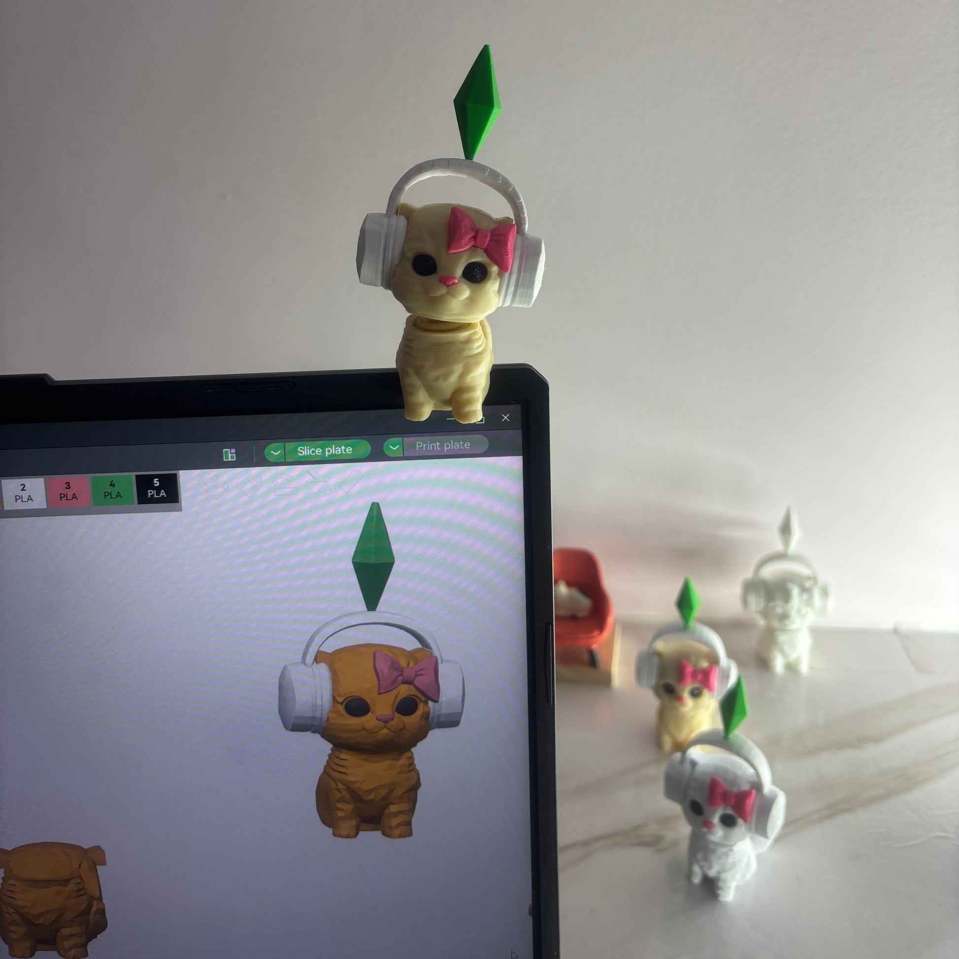 Toy figure of a bear with a green leaf on a white wall, with a computer screen displaying similar toy figure.