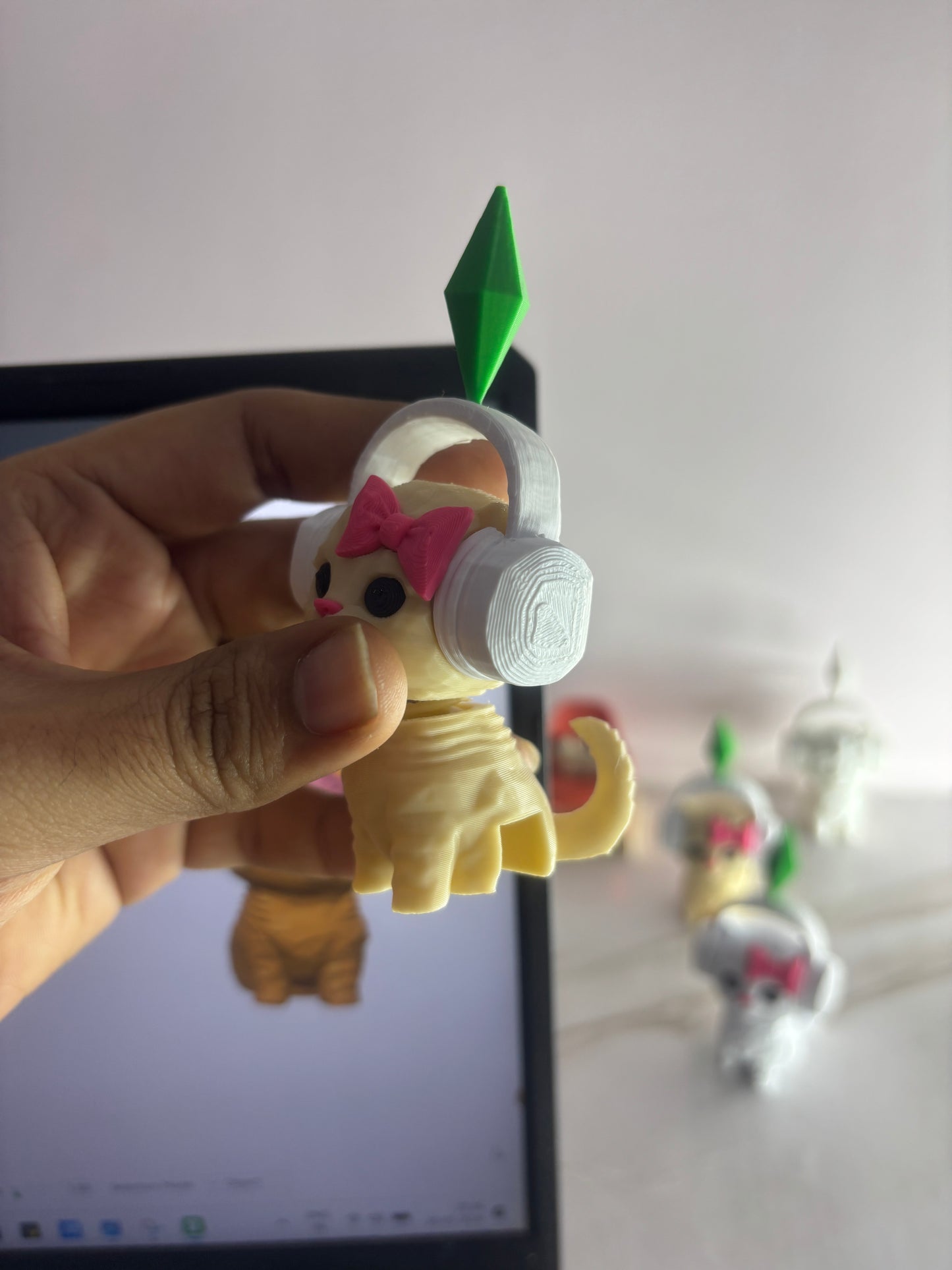 Small figurine with headphones held by a hand in front of a laptop screen