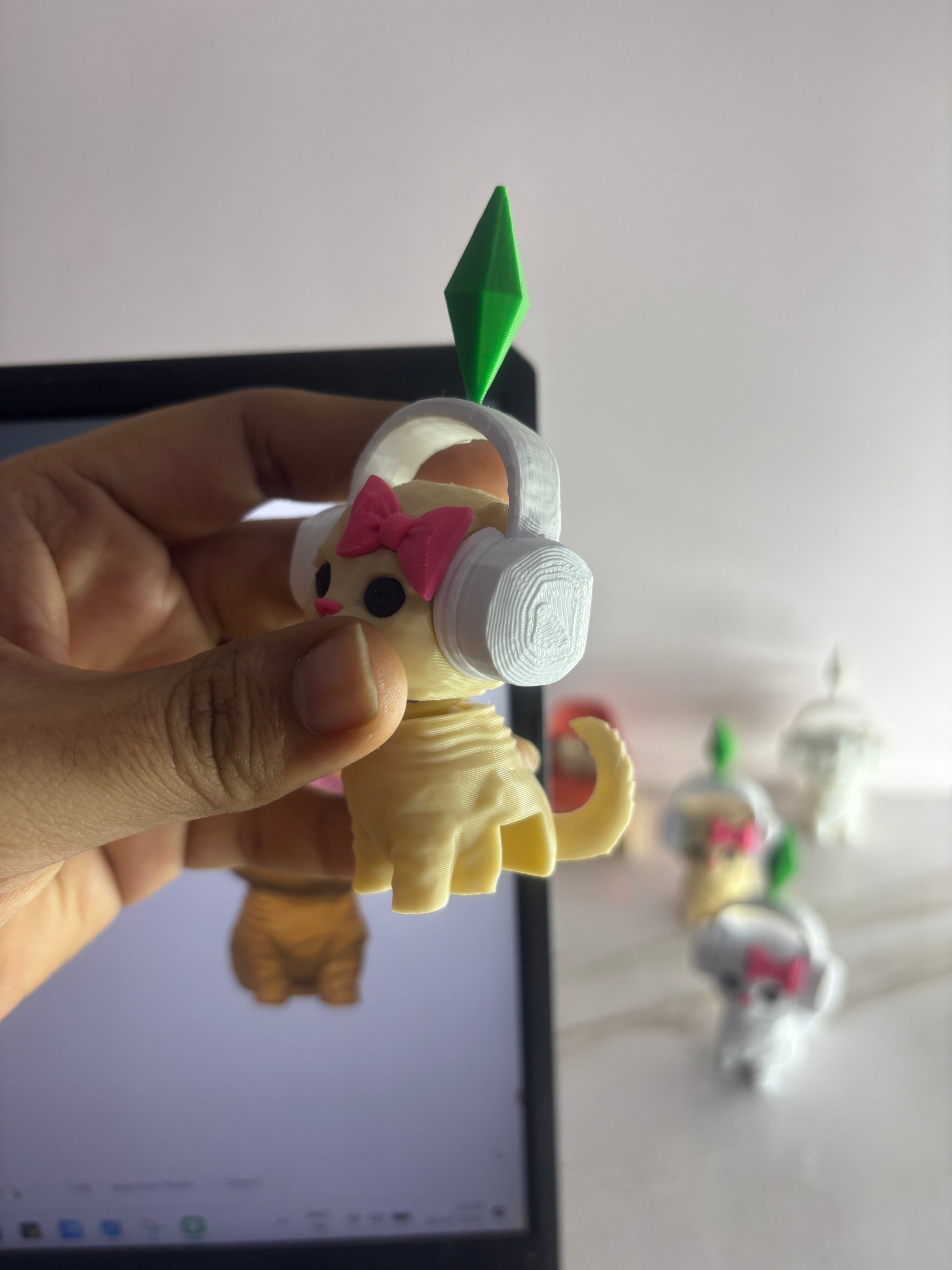 Small figurine with headphones held by a hand in front of a laptop screen