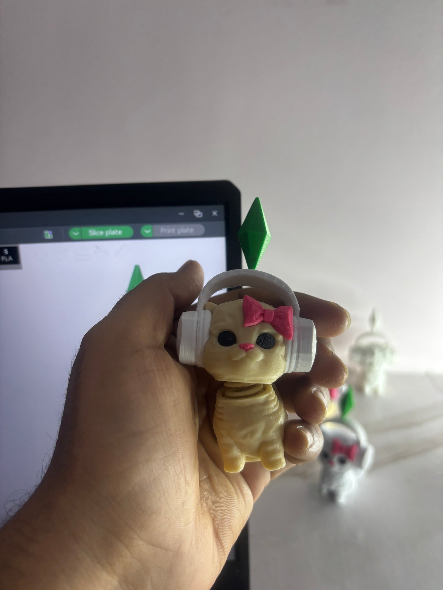 Hand holding a small plush toy with headphones and a bow tie in front of a computer screen.