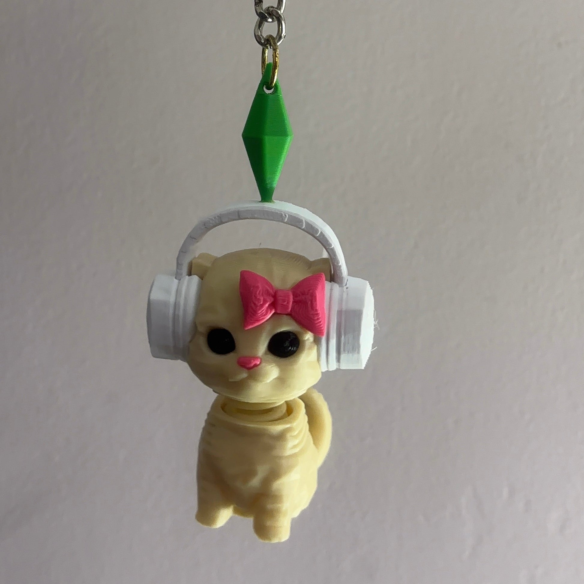 Keychain with a cat wearing headphones and a pink bow, hanging from a hook.