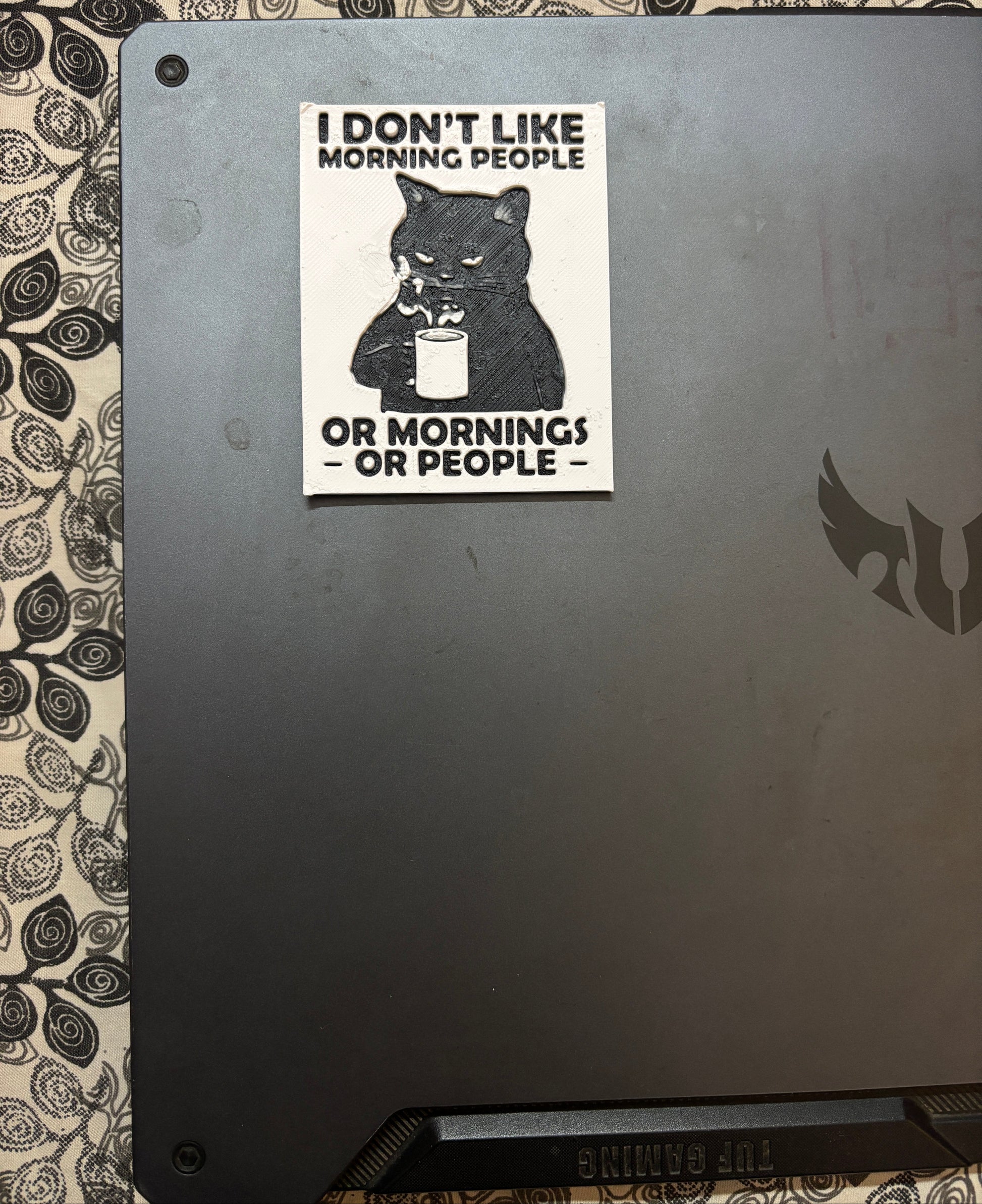 Sticker on a laptop with text 'I don't like morning people or morning people or morning people' on a decorative surface.
