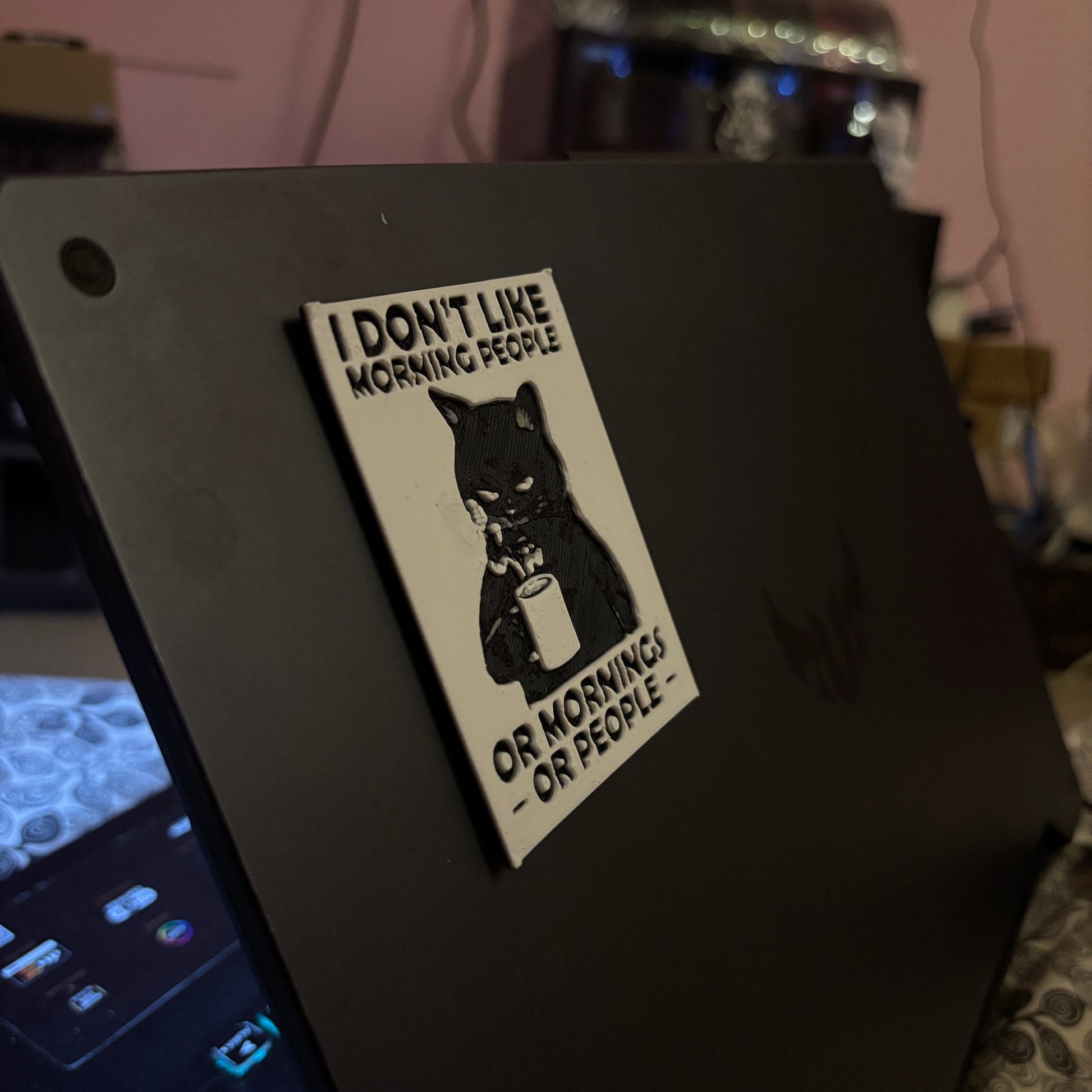 Sticker on a laptop with text 'I don't like morning people or mornings or people' on a dark background.